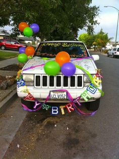 a white car with balloons and streamers on it's hood is parked in the street