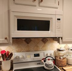 a microwave above the stove in a kitchen with utensils and other items on the counter