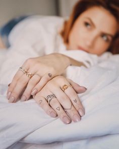 a woman is laying in bed with her hands on the pillow and two different rings