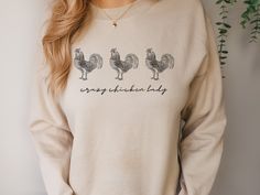 Chicken Sweatshirt, Crazy Chicken Lady, Farm Animal Lover Gift, Women Chicken Sweatshirt, Chicken Lover Sweatshirt Stay cozy and stylish with this funny chicken sweatshirt! Made from a soft and comfortable cotton-polyester blend, this sweatshirt features a cute rooster design that is sure to make you smile. Perfect for anyone who loves farm animals or just wants to add some humor to their wardrobe. This sweatshirt is available in a range of sizes, and comes in a variety of colors to suit your personal style. It is machine washable and easy to care for, so you can wear it again and again. Whether you wear it to the farm or just around town, this chicken sweatshirt is a must-have for any animal lover. // 50% cotton, 50% polyester blend // Medium-heavy fabric // Loose fit // Runs true to size Chicken Sweatshirt, Rooster Design, Crazy Chicken, Crazy Chicken Lady, Chicken Lady, Chicken Shirts, Funny Chicken, Lover Sweatshirt, Cute Chickens