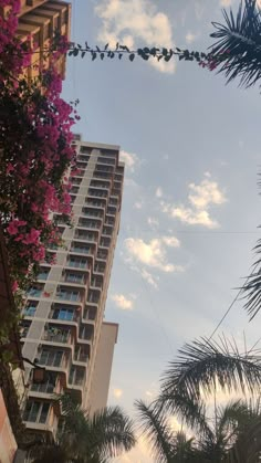 a tall building with lots of windows next to palm trees and flowers in the foreground