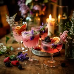 two glasses filled with drinks sitting on top of a table next to flowers and candles