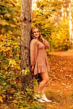 a beautiful young woman leaning against a tree in an autumn forest with leaves on the ground