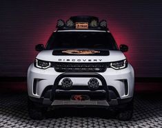 the front end of a white land rover with its lights on and an orange light behind it