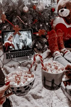 a teddy bear sitting in front of a christmas tree next to two buckets of marshmallows