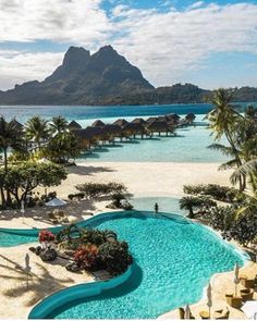 an outdoor swimming pool surrounded by palm trees and blue water with mountains in the background