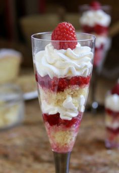 a dessert with strawberries and almonds in a glass on top of a wooden table