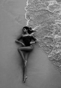 a woman laying on top of a sandy beach next to the ocean with waves coming in