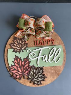 a happy fall sign hanging from the side of a wall with leaves and ribbons on it