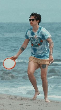 a man on the beach holding a frisbee in his hand and wearing sunglasses