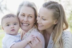 a woman holding a baby and smiling at the camera with her arm around another woman's shoulder