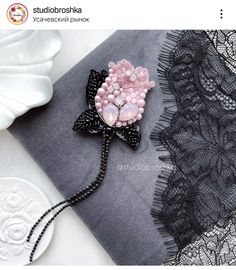 a pink flower brooch sitting on top of a black lace table cloth next to a white plate