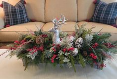 a christmas centerpiece with pine cones, evergreens and red berries sits on a table in front of a couch