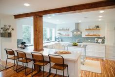 a kitchen with wooden floors and white cabinets is seen from across the room, there are four bar stools at the center of the island