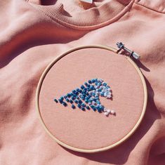 a close up of a embroidery on a pink shirt with blue beads in the shape of a bird