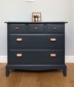 a black dresser with copper handles in a white walled room next to a wooden floor