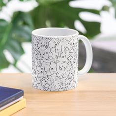 a white coffee mug sitting on top of a wooden table next to a book and plant