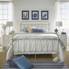 a white bed sitting in a bedroom next to two windows with blue and white decor