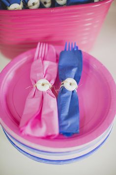 two pink and blue plates with silverware on them next to a bowl full of white buttons