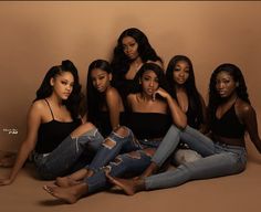 four women sitting on the floor posing for a photo together, with one woman wearing ripped jeans