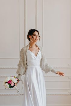 a woman in a white dress and cardigan posing for the camera with her hands out