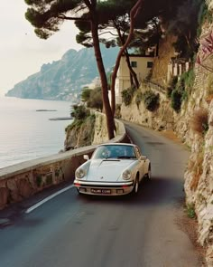 a white car driving down the road next to some trees and water with mountains in the background