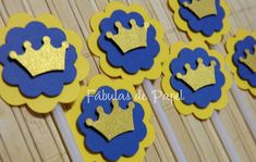 some blue and yellow cupcake toppers with gold crowns on them, sitting on a bamboo mat