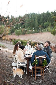 a group of people sitting at a table with a dog standing next to the table