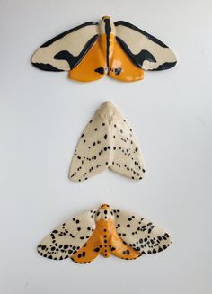 three ceramic moths on a white surface with black dots and orange spots, each flying in the same direction