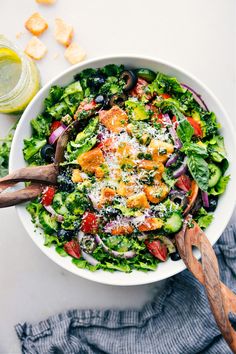 a salad in a white bowl with wooden serving utensils on the side next to it