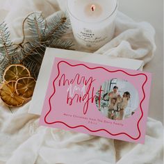 a christmas card sitting on top of a white blanket next to a candle and some pine branches