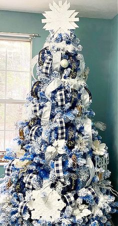 a blue and white christmas tree decorated with snowflakes, bows and ornaments in a living room