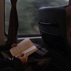 a person sitting on a train with a book in their hand and looking out the window