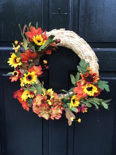 a wreath with sunflowers and other flowers hanging on the front door to decorate it