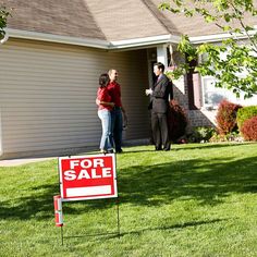 a real estate for sale sign in front of a house with two people standing outside