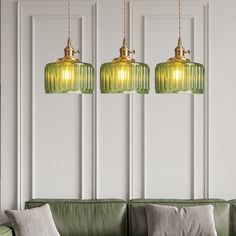 three green glass pendant lights hanging over a couch