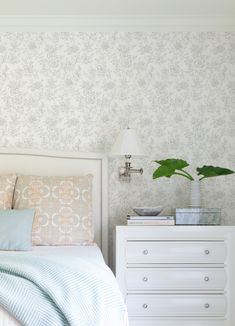 a white bed sitting next to a dresser with a plant on it's headboard