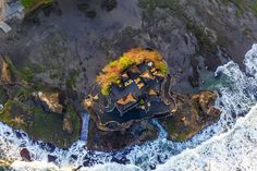 an aerial view of a house on the rocks by the ocean with waves crashing around it