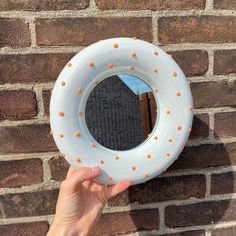 a hand holding up a white life preserver against a brick wall with orange dots