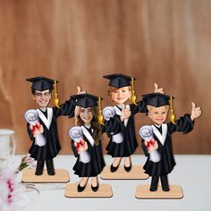 four children in graduation caps and gowns are standing on wooden bases with their thumbs up