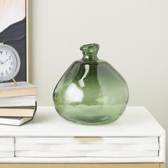 a green vase sitting on top of a white table next to a stack of books