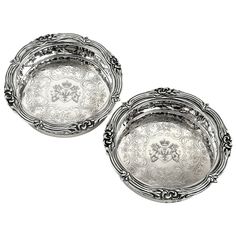 two silver trays sitting next to each other on a white surface with an ornate design