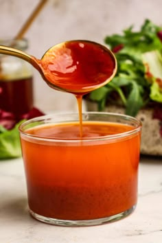 a spoon full of sauce being poured into a glass bowl with lettuce in the background