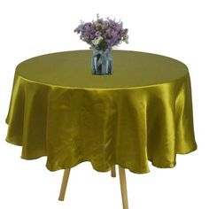 a vase with flowers on top of a yellow round table cloth covered by wooden legs