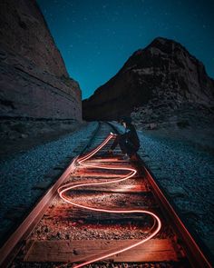 a person sitting on train tracks at night with their arms crossed and lights glowing in the dark