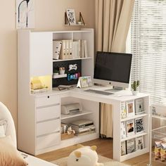 a white desk with a computer on it in a room next to a bed and window