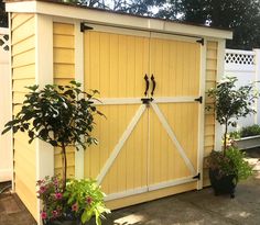 a yellow shed with two doors and some potted plants