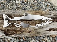 a metal fish cut out on top of a piece of driftwood next to some rocks