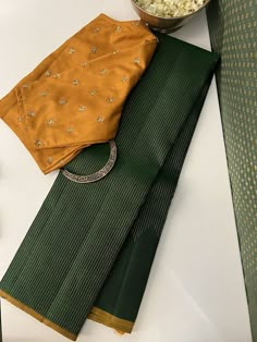 A gorgeous green monotoned pure handwoven kanchipuram silk saree with a beautiful mustard selvedge and blouse may seem simple at first glance but the magic is all packed into the pure zari work thats so intricately and thoughtfully done on it. Delicate pure zari threads gradually ascend along the border, reaching their peak at the pallu. In an unexpected twist, the pallu is with traditional muthu lines , adding a unique touch to its elegance. Green Mysore Silk Saree, Green Saree Contrast Blouse, Simple Silk Saree, Contrast Colour Combination, Kerala Saree Blouse Designs, Sleeveless Blouse Designs, Saree Styling