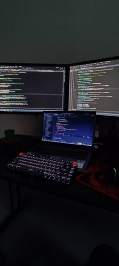 two computer monitors sitting next to each other on top of a black desk in front of a dark wall